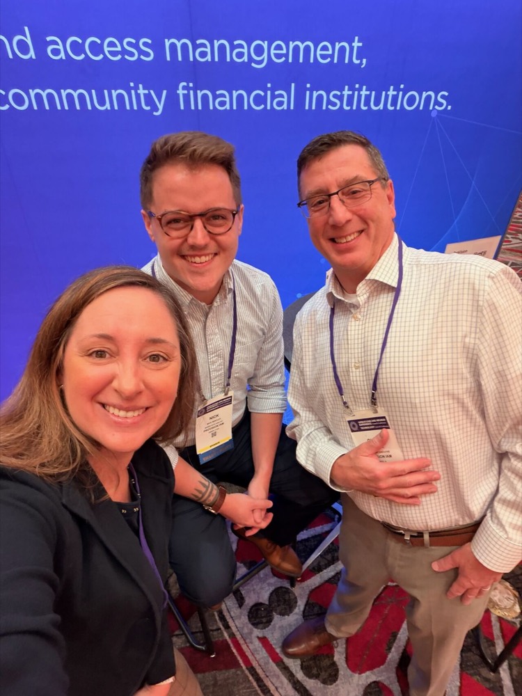 Three members of the Provision IAM team smiling in front of the Provision booth backdrop.