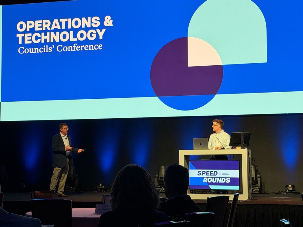 Two presenters on stage at the Operations and Technology Councils’ Conference, with a Speed Rounds sign on the podium.